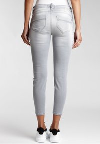 Jeans grises ajustados con una textura suave, corte slim y bolsillos traseros con parche. Usados con zapatillas blancas y negras.