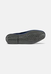 Suela de zapato con material de goma negra, superficie texturizada y costuras blancas; forma curvada con punta redondeada para mayor flexibilidad.