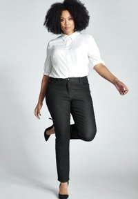Camisa blanca de botones, jeans ajustados negros y tacones negros. Tejido suave, ajuste entallado, mangas cortas y un cuello puntiagudo.