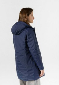 Giubbotto imbottito blu navy con cappuccio, caratterizzato da una texture trapuntata, chiusura frontale con zip e tasche laterali, progettato per calore e comfort.