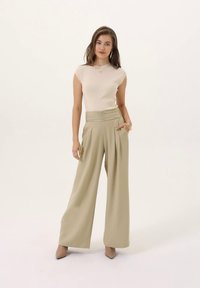 Top bege sem mangas com texturas em relevo, combinado com calças verde-oliva de cintura alta e perna larga. Textura suave com pregas, complementado com saltos beges pontiagudos.