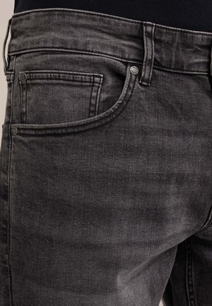 Čierne denimové rifle s vyblednutou textúrou, vybavené prednou vreckom a kovovými gombíkmi. Pás je jednoduchý bez ďalších ozdôb.