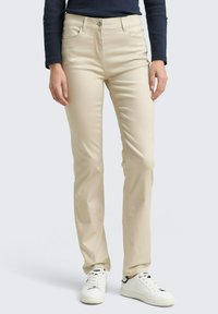 Beige katoenen broek in een slim fit, met een vijf-zakken ontwerp en sluiting met een knoop, gedragen met witte sneakers.