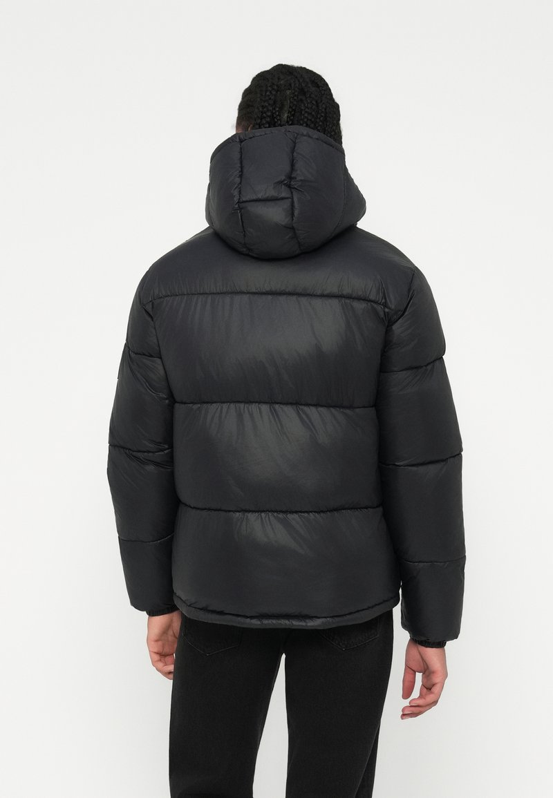 Veste matelassée noire avec capuche, présentant un design matelassé, une texture lisse et des poignets élastiques, vue de dos.