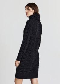 Vestito dolcevita nero a maglia a trecce con polsini a coste e motivo testurizzato, progettato per una silhouette aderente che arriva a metà coscia.