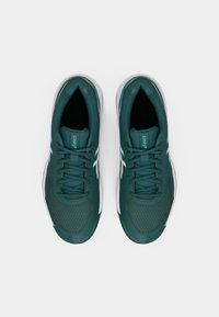 Teal idrettssko med teksturert overdel, snøring, og hvite detaljer langs sidene. Myke materialer og polstret innside.