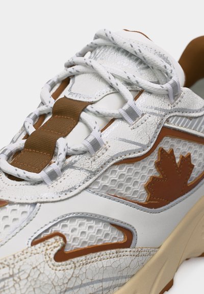 Baskets blanches et marron avec texture craquelée, panneaux en maille à treillis, passants pour lacets, et un motif de feuille d'érable marron sur le côté.