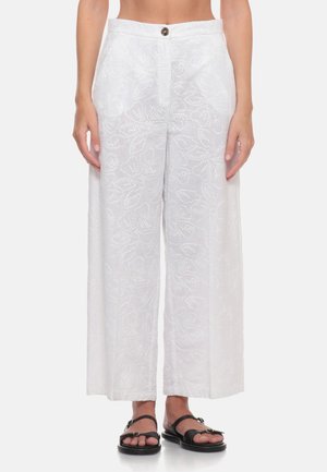 Pantaloni bianchi a vita alta, gamba larga con ricamo floreale sottile, chiusura frontale con bottoni, indossati con sandali neri con punta aperta.
