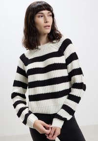 Maglione lavorato a maglia con righe orizzontali bianche e nere, scollatura rotonda e polsini a coste. Texture spessa con vestibilità rilassata.