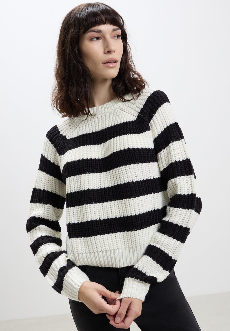 Maglione lavorato a maglia con righe orizzontali bianche e nere, scollatura rotonda e polsini a coste. Texture spessa con vestibilità rilassata.