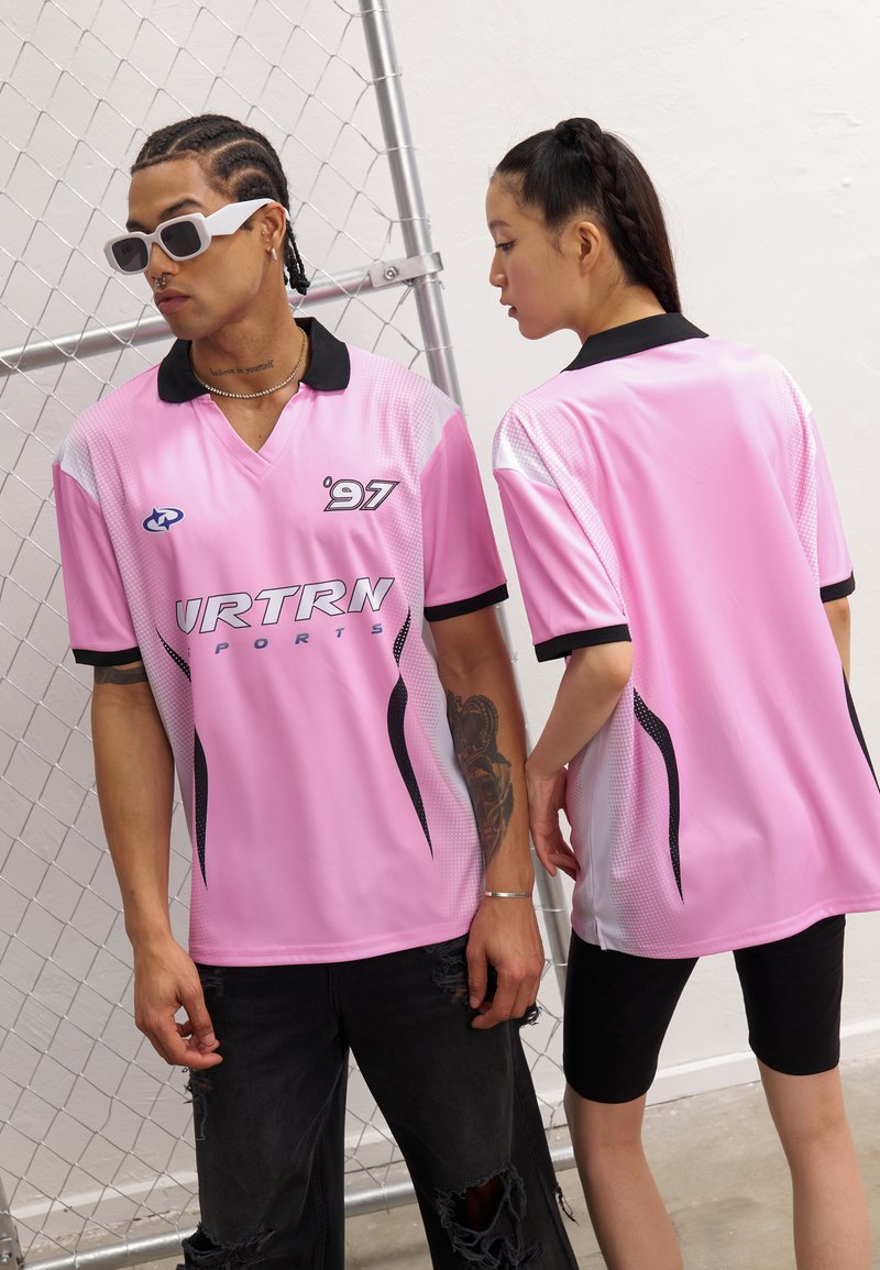Roosa spordijerseys mustade aktsentidega, lühikeste varrukatega ja V-kaelusega. Esiküljel on logo ja graafiline disain. Tekstuuriga külgpaneelid.