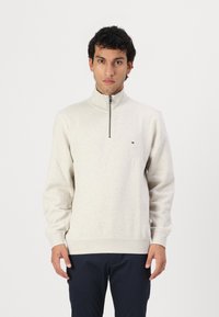 Lichtgrijze zip-neck sweater met lange mouwen, geribbelde manchetten en zoom, met een klein logo op de borst. Zachte katoenmix stof.