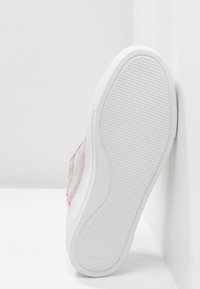 Sneaker z jasnoszarej zamszowej cholewki z różowym akcentem oraz białą fakturowaną gumową podeszwą, przedstawiony z perspektywy podeszwy.