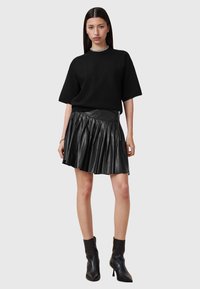 Sudadera negra de manga corta combinada con una falda corta de cuero con plisados negra. La falda cuenta con un cierre lateral y una textura estructurada. Botines negros.
