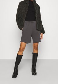 Shorts gris en tissu doux avec une taille élastique, associés à une veste sombre en peluche et des bottes en cuir noires montant jusqu'aux genoux.