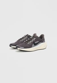 Baskets athlétiques noires et grises avec une tige en maille, un col rembourré et une semelle légère. Présente un logo swoosh noir bien visible sur le côté.