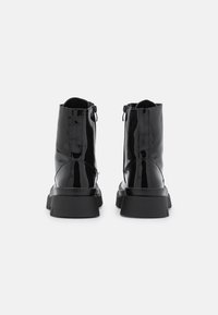 Bottines noires en cuir verni avec un bout rond et une semelle en caoutchouc épaisse, dotées d'une fermeture éclair latérale pour un enfilage facile. Texture lisse et finition élégante.