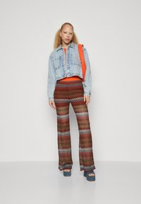 Denim skraćena jakna u svijetloplavoj boji, narančasta majica i šarene hlače s zvonastim nogavicama koje sadrže crvene, smeđe i srebrne pruge; uparen s plavim platformama.