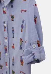 Camicia azzurra chiara in cotone, con grafiche di orsi colorati e la parola "guess" in rosso. Bottoni bianchi sui polsini.
