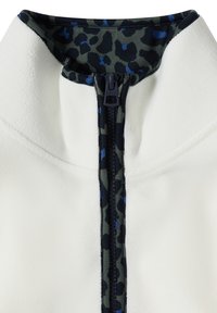 Veste en polaire blanche avec fermeture éclair centrale et bordure imprimé léopard bleu foncé et gris autour du col et de la fermeture éclair.