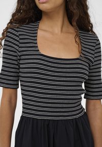 Črno-bela obleka z navpičnimi črtami, kvadratnim izrezom, rebrasto teksturo zgornjega dela in tekočim črnim spodnjim delom.