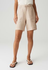 Pantaloni corti in lino beige con vita elastica, cordoncino e due tasche anteriori. Il tessuto ha una finitura naturale e testurizzata.