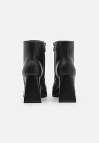 Botines de cuero negro hasta el tobillo con un alto tacón bloque, cremallera lateral y textura suave. Presentan una silueta elegante y acentos mínimos.