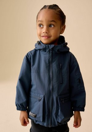 Tumši zila bērnu jaka ar kapuci, elastīgām aprocēm, priekšējo rāvējslēdzēju un vairākām rāvējslēdzēja kabatām. Gluda tekstūra, viegls audums.