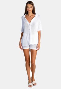 Vit stickad knapp-up topp med kort ärm, parat med vita shorts, med en lös passform och andningsbar textur. Bärs med ljusa sandaler.