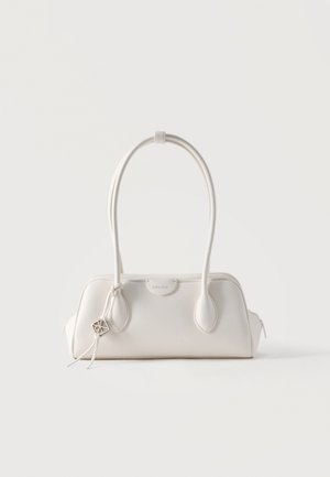 Petit sac à main en cuir blanc avec deux longues anses, un pendentif logo argenté et une fermeture éclair de chaque côté, posé sur un fond blanc uni.