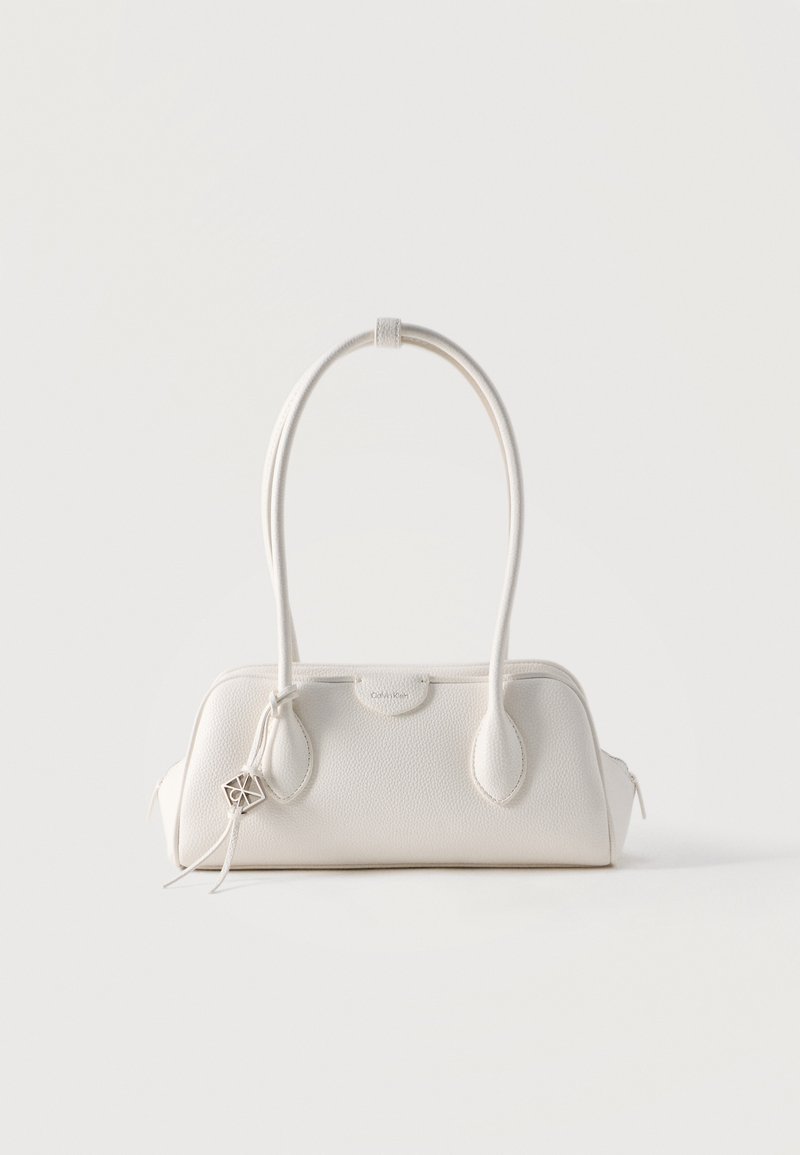 Μικρή λευκή δερμάτινη τσάντα χειρός με δύο μακριές λαβές, ασημένιο λογότυπο-γούρι και κλείσιμο με φερμουάρ σε κάθε πλευρά, τοποθετημένη πάνω σε λευκό απλό φόντο.