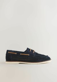 Mocassin en cuir tressé bleu marine avec détails de lacets beige et semelle blanche, présenté en profil latéral sur un fond neutre.
