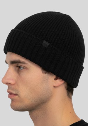 Zwarte gebreide beanie met een geribbelde textuur en een opgerolde rand. Heeft een klein label aan de zijkant, ontworpen voor warmte en comfort.