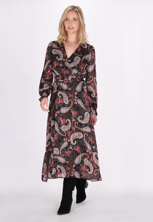 Maxi dress nero con stampa paisley e dettagli floreali rossi, caratterizzato da maniche lunghe, scollo a V e vita aderente, abbinato a stivali neri al ginocchio.