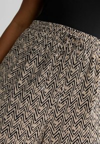 Beige Hosen mit elastischem Bund und einem schwarzen Zickzackmuster. Verfügt über einen Kordelzugverschluss und eine glatte, leichte Stofftextur.