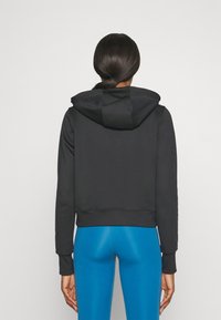 Sudadera negra corta con acabado texturizado, con capucha, puños y dobladillo acanalados. Combinada con leggings azules ajustados.