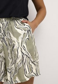 Shorts verts et blancs à motif, de coupe décontractée, avec une taille élastique et des poches latérales, fabriqués dans un tissu léger.