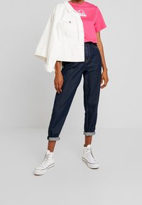 Chaqueta de mezclilla blanca, camiseta gráfica rosa, jeans oscuros de tiro alto con dobladillo y zapatillas altas blancas. Diseño simple con colores contrastantes.
