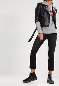 Giacca da biker in pelle nera sopra un hoodie grigio, abbinata a jeans neri a vita alta e stivali neri lucidi alla caviglia. Presenta cerniere e una vita con cintura.