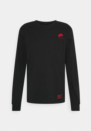 T-shirt noir à manches longues Nike Air avec un logo rouge sur la poitrine gauche et une petite étiquette rouge et noire près de l'ourlet inférieur.