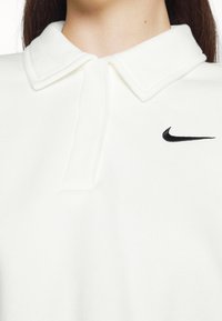 Polo blanco de tela suave con cuello doblado y un logo de Nike bordado en negro en el área izquierda del pecho.