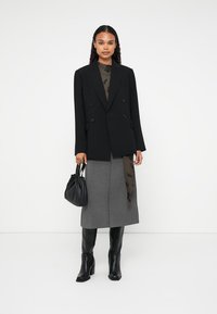 Blazer nero doppiopetto, gonna midi grigia, stivali neri al ginocchio e sciarpa testurizzata. Tieni in mano una borsa nera con cordino.
