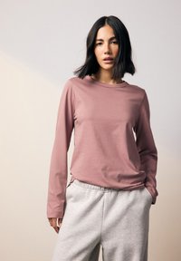 Rosa långärmad tröja i mjukt tyg med rund halsringning, kombinerad med ljusgrå joggingbyxor med elastisk midja och fickor.