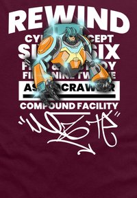 Bordová látka má grafický design s modrou a oranžovou robotickou postavou nad bílým textem, který zahrnuje slova "REWIND" a "COMPOUND FACILITY."