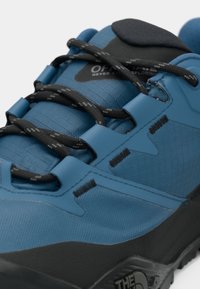 Μπλε πεζοπορικό παπούτσι με υφασμάτινο άνω μέρος με υφή, μαύρα κορδόνια και σκληρή ελαστική σόλα. Διαθέτει λογότυπο στο πλάι και μοναδικό σχεδιασμό κλειδώματος κορδονιών.