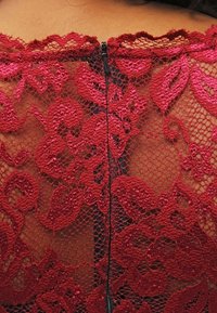 Tissu en dentelle rouge avec des motifs floraux, présentant une fermeture éclair noire visible à l'arrière, mettant en valeur la texture et le design délicats de la dentelle.