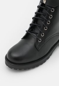 Schwarze Leder-Schnürstiefel mit runder Spitze, Metallösen und dickem profiliertem Absatz auf einem wei�ßen Hintergrund.