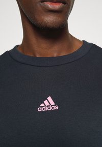 Close-up of a dark sweatshirt featuring a pink Adidas logo on the chest, highlighting its texture and collar detail.