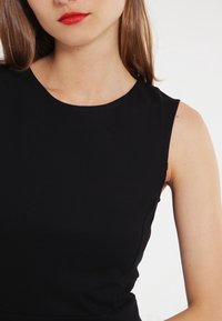 Czarny bezrękawnik z okrągłym dekoltem, gładką fakturą i dopasowanym krojem, prezentujący czystą i minimalistyczną sylwetkę.