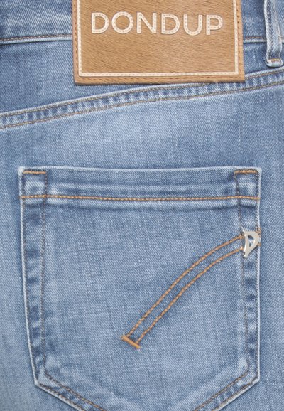 Jean en denim bleu clair avec une patch en cuir marron de marque, présentant une petite poche cousue avec un détail en argent et un fil contrastant.
